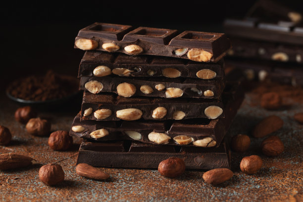 黑巧克力和牛奶巧克力，坚果在深色背景上撒上可可粉。图片下载