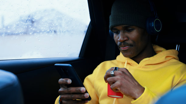 一个穿着运动服的男人坐在车里，喝着咖啡，用智能手机浏览社交网络图片下载