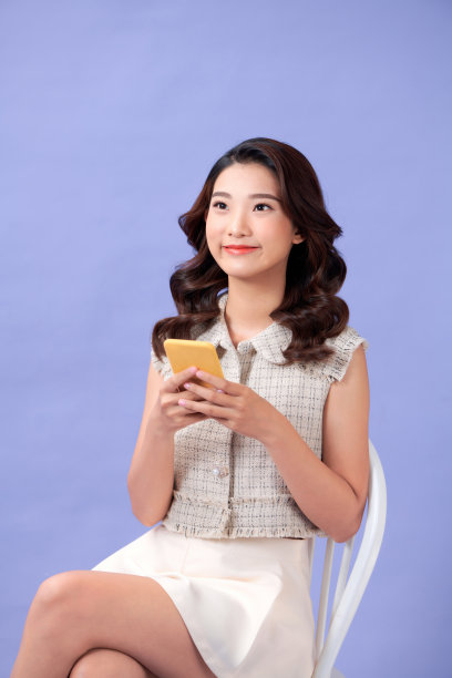 拿着智能手机的年轻女子坐在紫色背景的椅子上图片下载