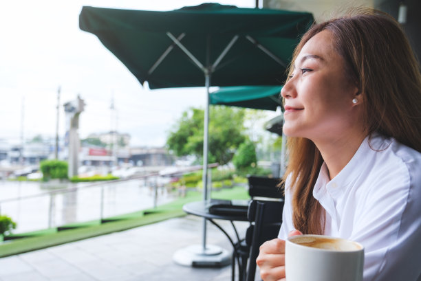 一个美丽的年轻亚洲女子在户外咖啡馆拿着热咖啡喝的特写照片图片下载