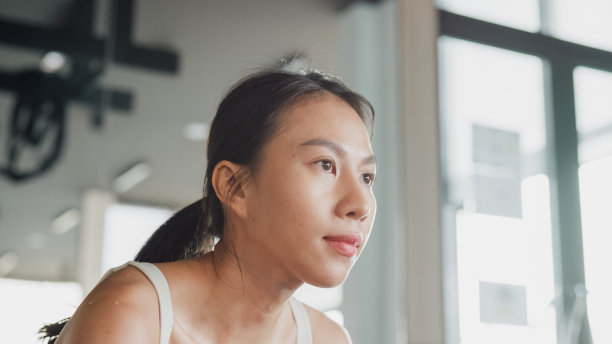 现代健身房里，年轻的亚洲女运动员在运动，健美运动员在喝瓶装水。图片下载