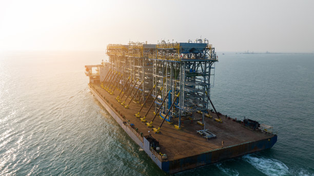 日落时分，驳船运输平台上的招标钻井平台到海洋中央的石油钻井平台。驳船运输油网的大型设备。图片下载
