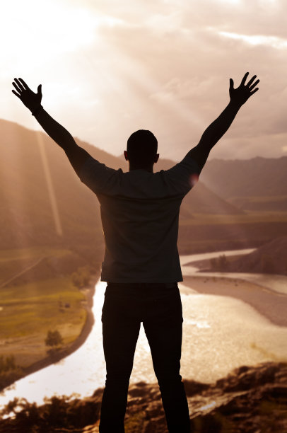 日落时分，一个男人在山顶上举起双手的剪影图片下载