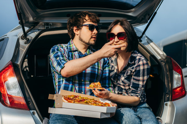 时髦的成年夫妇坐在汽车后备箱里，在户外吃披萨图片下载