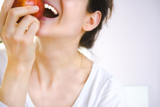 有着美丽笑容和洁白牙齿的年轻女子正在吃新鲜的红苹果图片下载