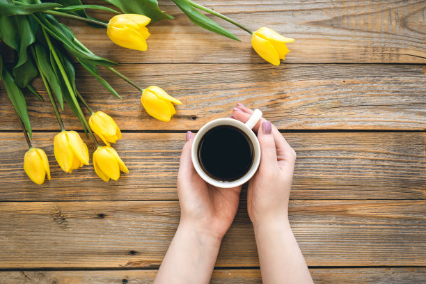 木制背景上的黄色郁金香花束和一杯咖啡，俯视图。图片下载