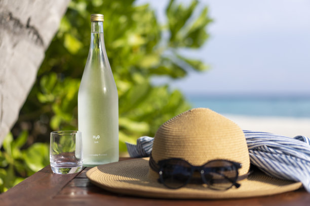 以马尔代夫海滩为背景的玻璃瓶、草帽和太阳镜图片下载