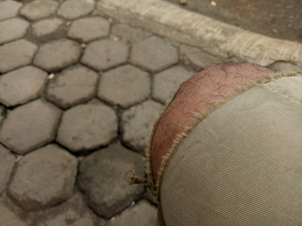 照片中，一个男孩的腿穿着破旧的棕色裤子，背景是六边形的砖地板图片下载