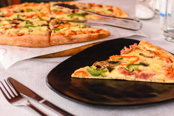 一块巨大的美味披萨，配上蘑菇、胡椒、奶酪和火腿，放在希腊酒馆外面的黑色盘子里。表设置。客户服务。地中海式饮食图片下载