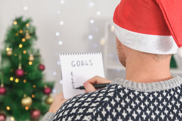 男子在白色的白板上写着圣诞装饰目标和新年和2023年圣诞节的计划。新年和圣诞节的目标写在黑板上。列出新年和圣诞节的愿望和目标。图片下载