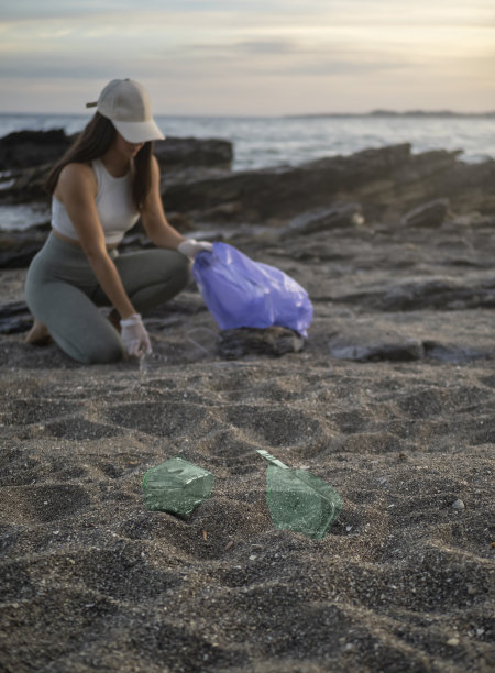 一个小女孩用一个蓝色的袋子从海滩上收集垃圾。塑料环境污染图片下载