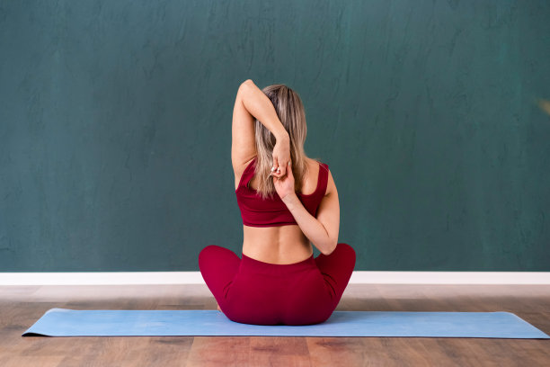 年轻女子在背后紧握双手，坐在瑜伽室的蓝色垫子上图片下载