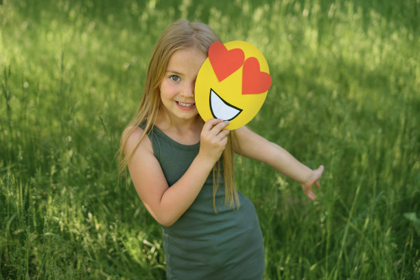 可爱的女孩拿着一张纸脸，上面有爱心而不是眼睛。图片下载