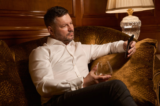 穿着正装的优雅商人拿着一杯白兰地在手机上打字图片下载