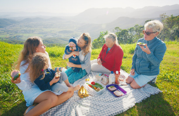 一个大家庭在日出时在山上的绿色小山上野餐图片下载