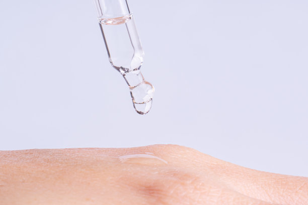 微距照片的妇女的手和移液管与油或凝胶。透明滴香精，油或凝胶从移液管滴在特别干燥的皮肤上图片下载