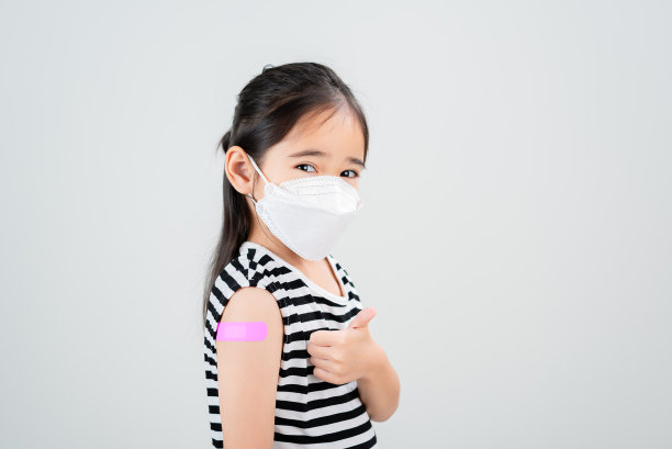 亚洲小女孩戴着医用口罩，在接种病毒疫苗后，她的手臂上缠着绷带。儿童和儿童疫苗接种运动。用疫苗概念保护你的孩子图片下载