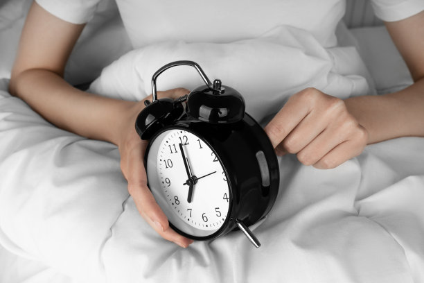 女人的手启动了床上的黑色闹钟图片下载