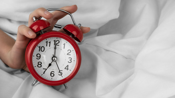 女人用手关掉床上的红色闹钟图片下载