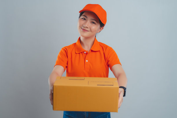 一名亚洲女子开心地微笑着，自信地穿着统一的polo t恤，向镜头递上一个纸箱，孤立地站在白色的背景上。图片下载