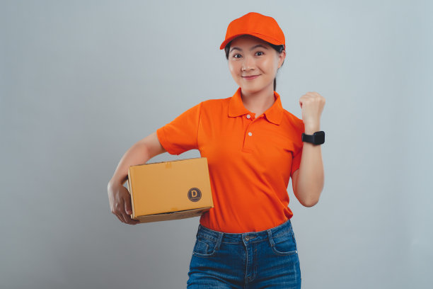 亚洲女人穿着统一的polo t恤，拿着箱子查看时间，很高兴能及时把包裹送到客户手中，孤立地站在白色的背景上。图片下载