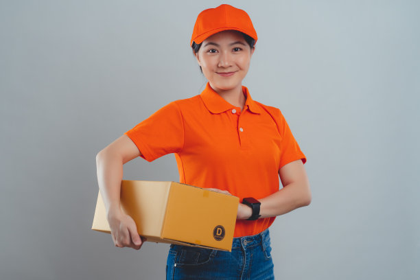 一名亚洲女子开心而自信地微笑着，穿着统一的polo t恤，拿着箱子站在白色的背景上。图片下载