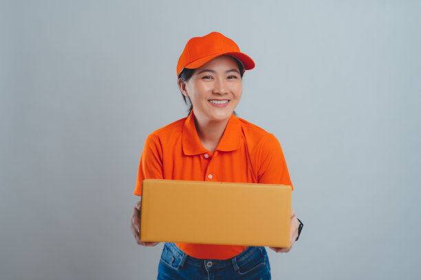 一名亚洲女子开心地微笑着，自信地穿着统一的polo t恤，向镜头递上一个纸箱，孤立地站在白色的背景上。图片下载
