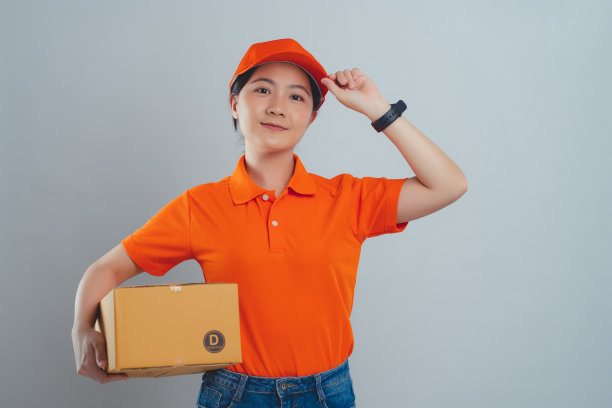 一名亚洲女子开心而自信地微笑着，穿着统一的polo t恤，拿着箱子站在白色的背景上。图片下载