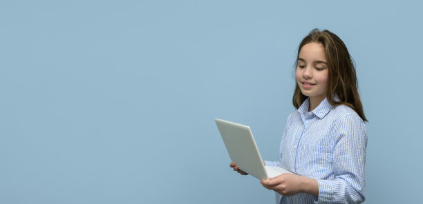 一个拿着蓝色背景白色笔记本电脑的女孩。横幅图片下载