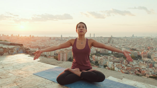黎明时分，身穿紧身衣的年轻女子在观景处练习瑜伽。女孩在莲花坐姿时举起双手图片下载