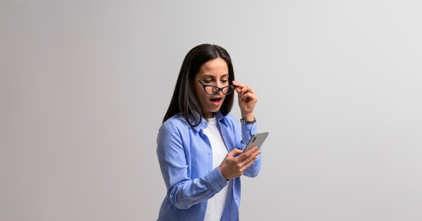 震惊的女性专业人士通过眼镜向外看，在手机上读到意想不到的信息。惊奇的女商人穿着便装查看社交媒体背景图片下载