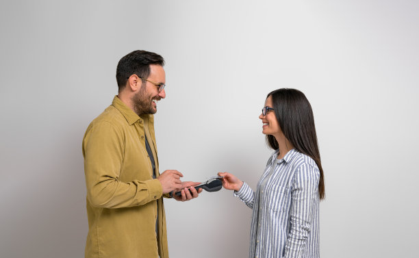 背景是男收银员手持的读卡机，微笑的女顾客在读卡机上刷卡的侧视图。男男女女推荐使用NFC技术进行无现金和非接触式交易图片下载