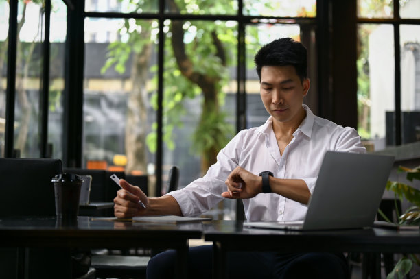 聪明的商人一边在咖啡店远程工作一边查看手表上的时间图片下载