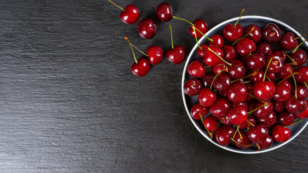 新鲜的红色成熟的甜樱桃与水珠盘黑色石板背景。图片下载
