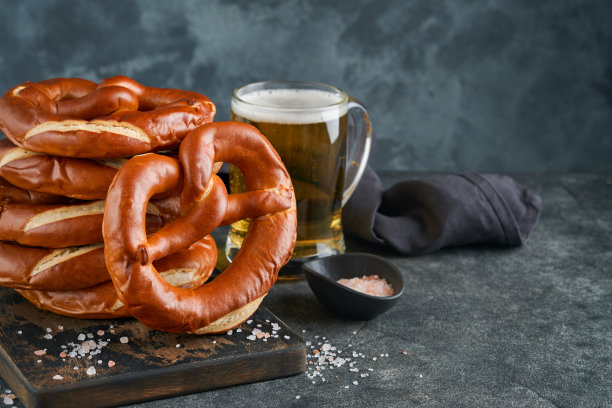 啤酒节概念卡。传统的巴伐利亚椒盐脆饼与啤酒瓶杯在古老的黑色乡村背景。非常适合十月节。啤酒节食物菜单。图片下载