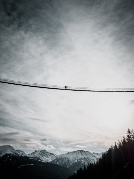 在多云的天空背景下，两个人在吊桥上的垂直拍摄图片下载