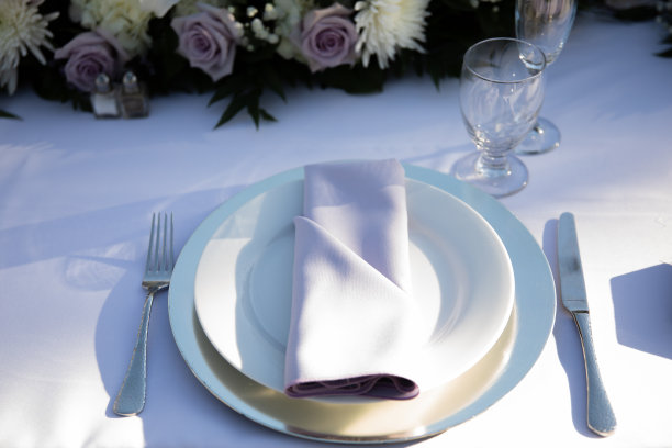 白色的盘子配上淡紫色的餐巾，清澈的酒杯和花朵——百合、玫瑰和菊花。婚宴桌图片下载