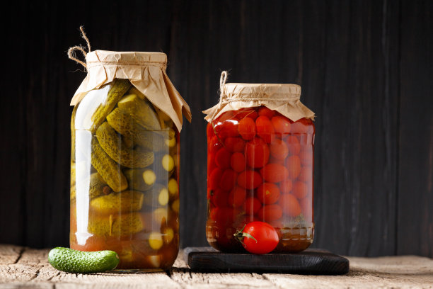 装在罐子里的罐装黄瓜和西红柿，背景是深色的木头。图片下载