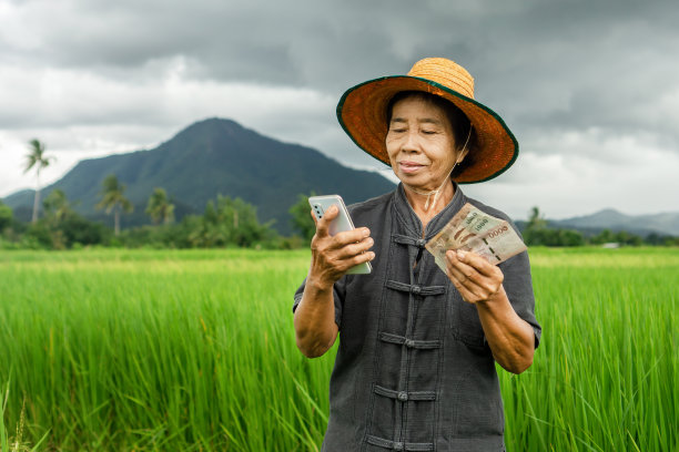 微笑的亚洲女农民手持泰铢钞票和手机领取现金补助图片下载