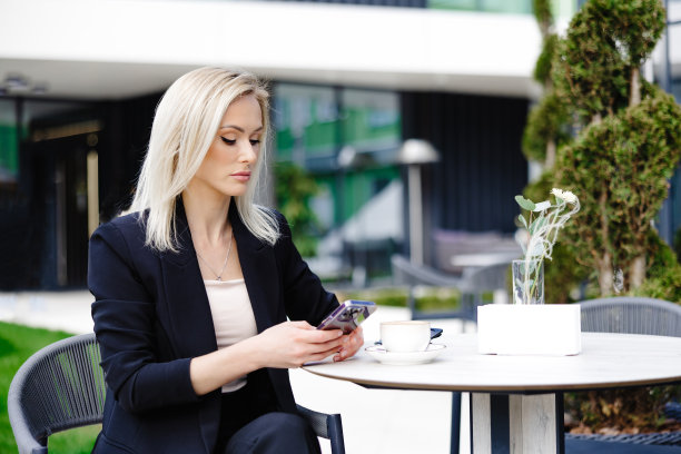 金发碧眼的商务女士看着手机，读着留言。女人正在露台上的咖啡馆里放松，享受着生活图片下载