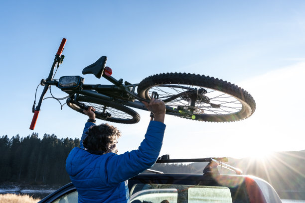 一个人骑完车后把自行车放到车上。图片下载