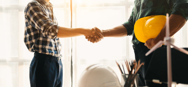 施工队握手问候，在办公室办公桌上戴着黄色头盔，开始新的工程计划，咨询他们的建筑工程。图片下载