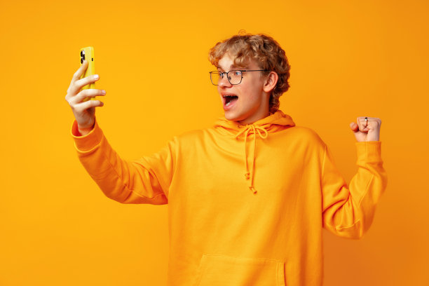 年轻人在手机上玩网络游戏的照片，背景是黄色图片下载