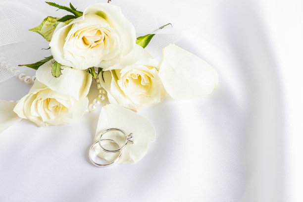 两枚美丽的白金钻石订婚戒指躺在茶叶花瓣上，背景是柔和的鲜花。一个拷贝空间。图片下载