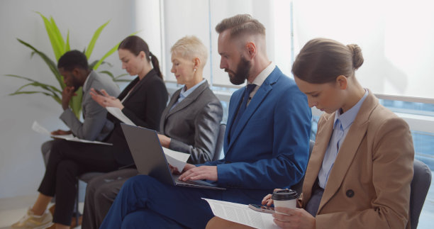 一群不同的商务人士带着文件和小工具坐在一排。图片下载