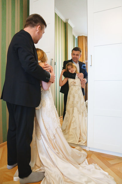 爸爸和穿着妈妈婚纱的金发小女孩站在镜子前。图片下载