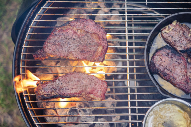 美味的牛排和肋眼烧烤股票照片。酱汁撒在肉上。烤架下面冒出了火图片下载