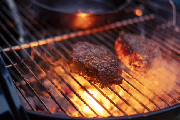 美味的牛排和肋眼烧烤股票照片。酱汁撒在肉上。烤架下面冒出了火图片下载