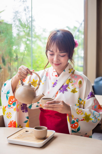 穿着传统和服的年轻女子坐在日式房子里倒茶喝，背景是花园图片下载