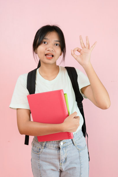 快乐的学生年轻的女孩拿粉红色的书和背包在粉红色的背景。图片下载